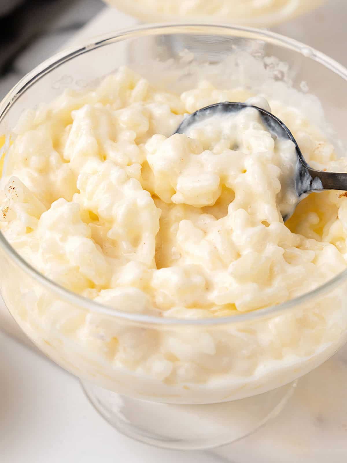 Creamy rice pudding in a glass cup with a dark metal spoon. Close up image. 