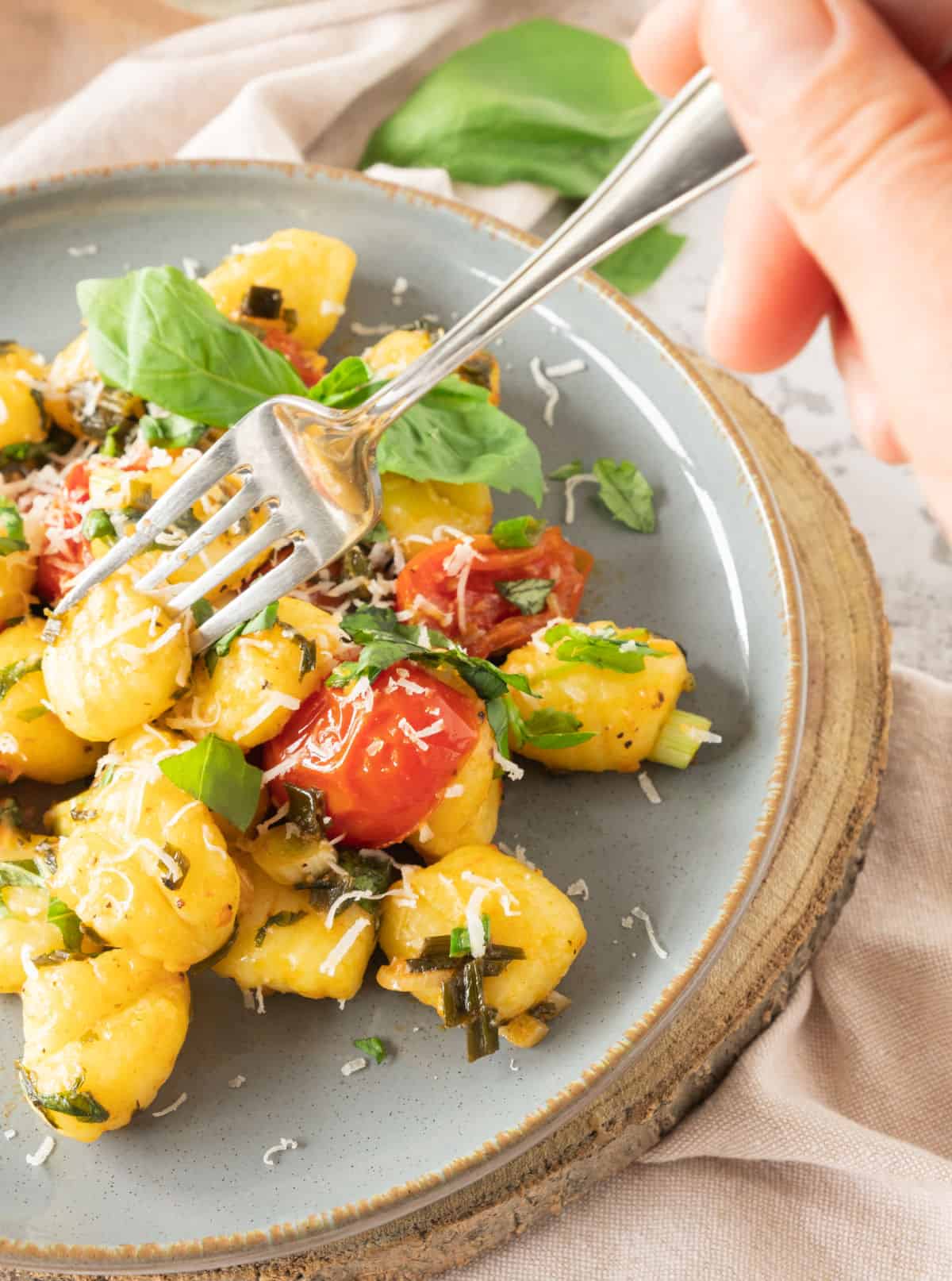 Forking potato gnocchi with basil and tomatoes in a grey plate. 