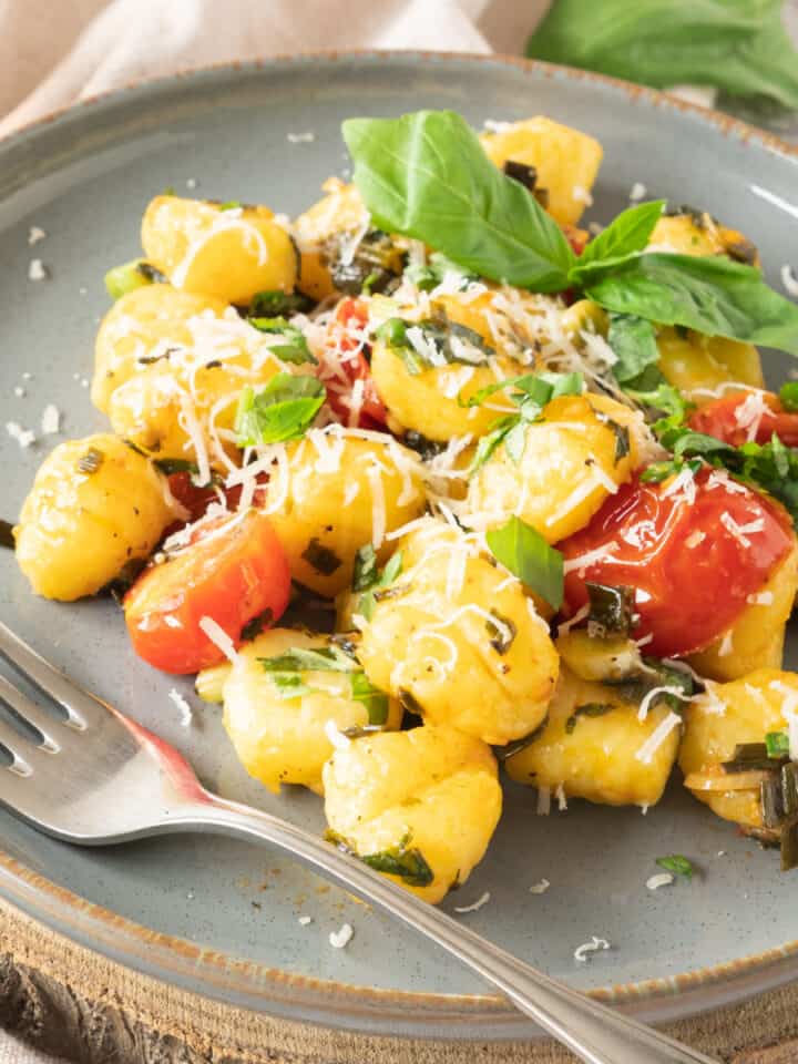 Grey plate with potato gnocchi serving with basil and tomatoes. A silver fork.