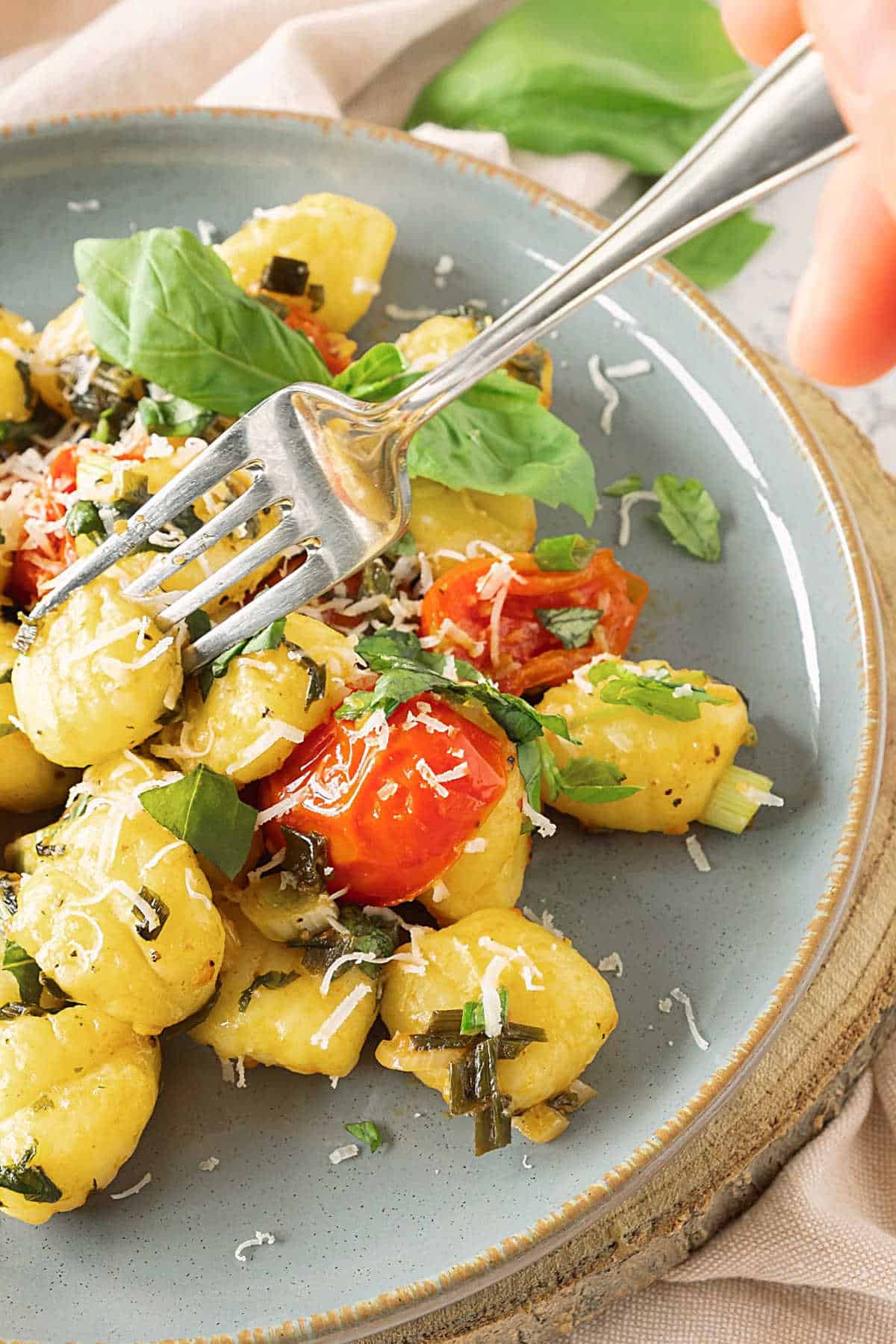 Forking tomato basil potato gnocchi on a grey plate.
