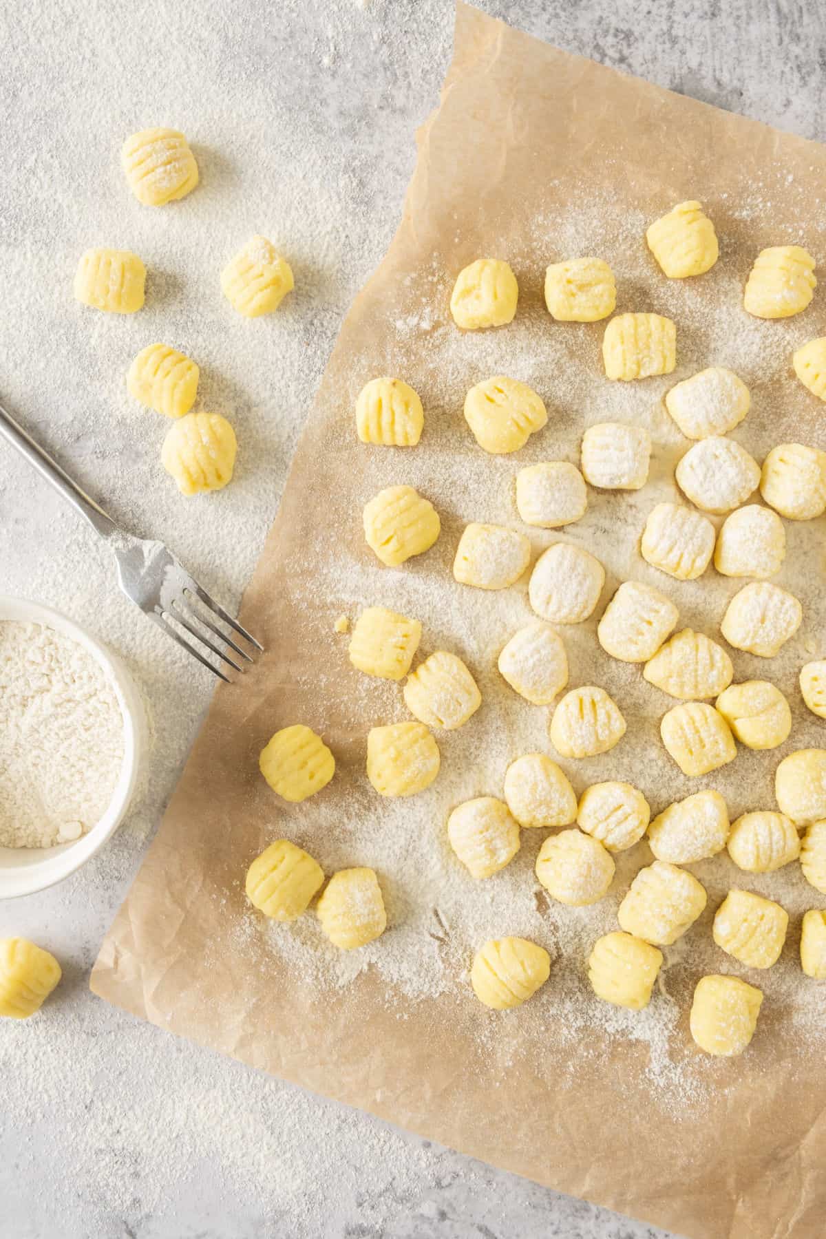 Beige parchment paper with raw potato gnocchi pieces. A fork.