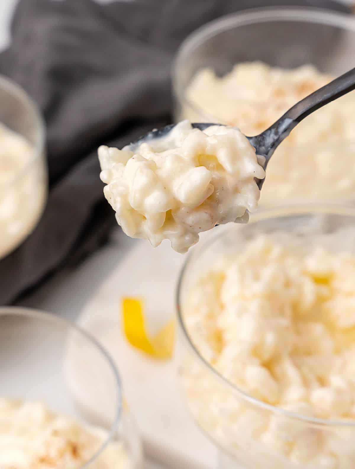 Rice pudding spooned with a dark metal spoon from a glass cup. Dark grey cloth in the background. 