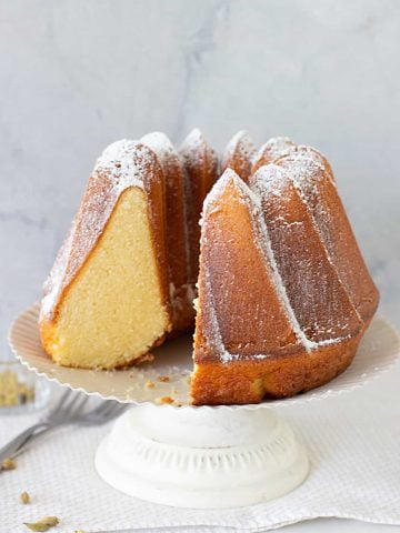 Cardamom Bundt Cake in a white cake stand, one piece missing