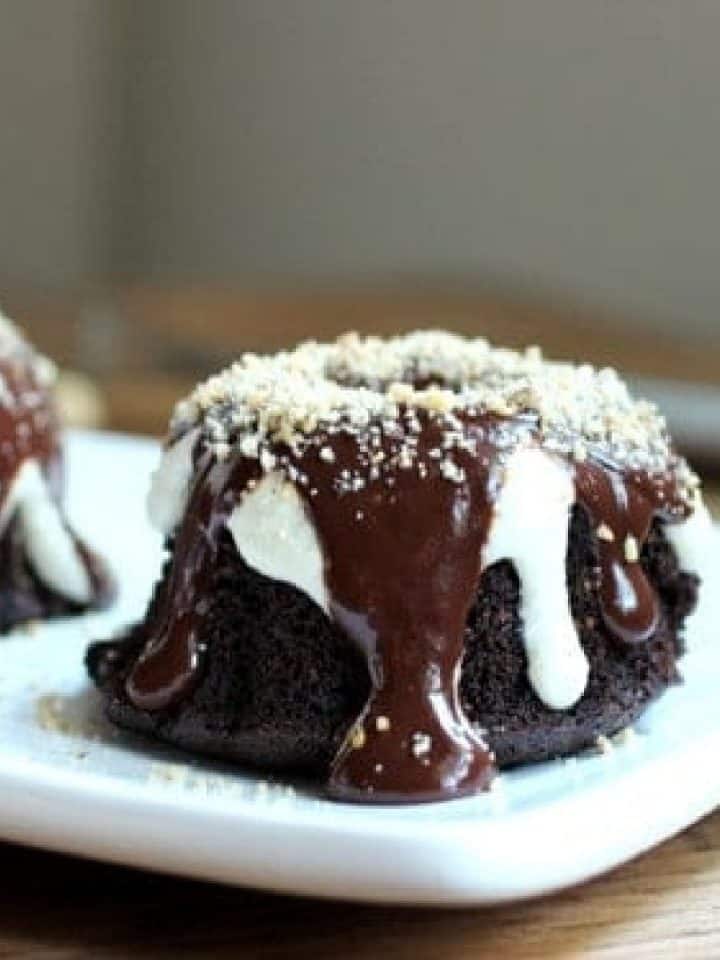 Small chocolate bundt cake on a white plate with white and dark icings.