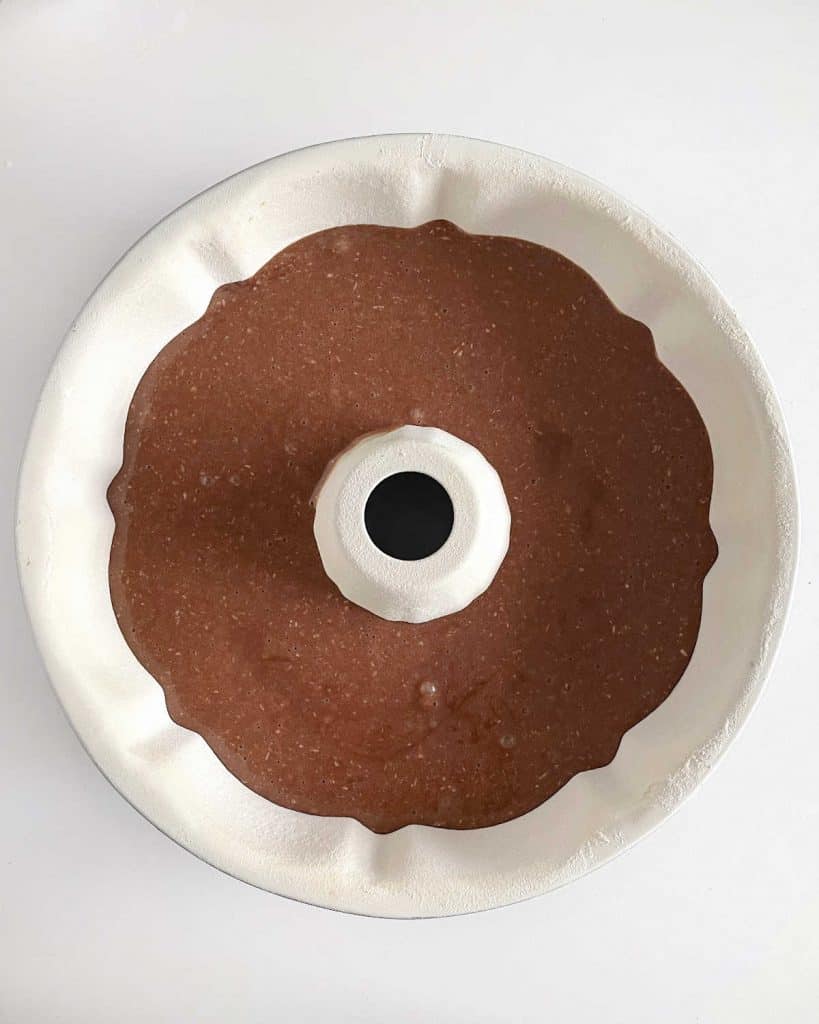 White bundt cake pan with chocolate cake batter. White surface. Top view.