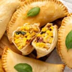 Two corn empanada halves with whole ones. Basil leaves.