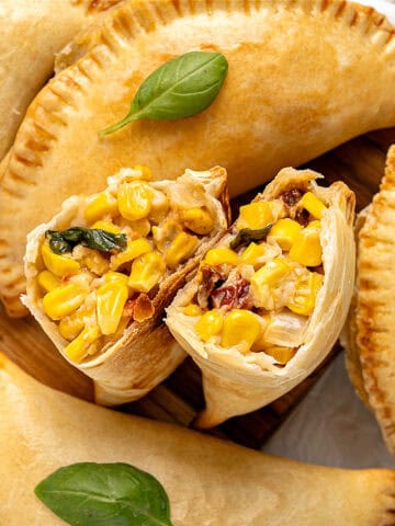 Two corn empanada halves with whole ones. Basil leaves.