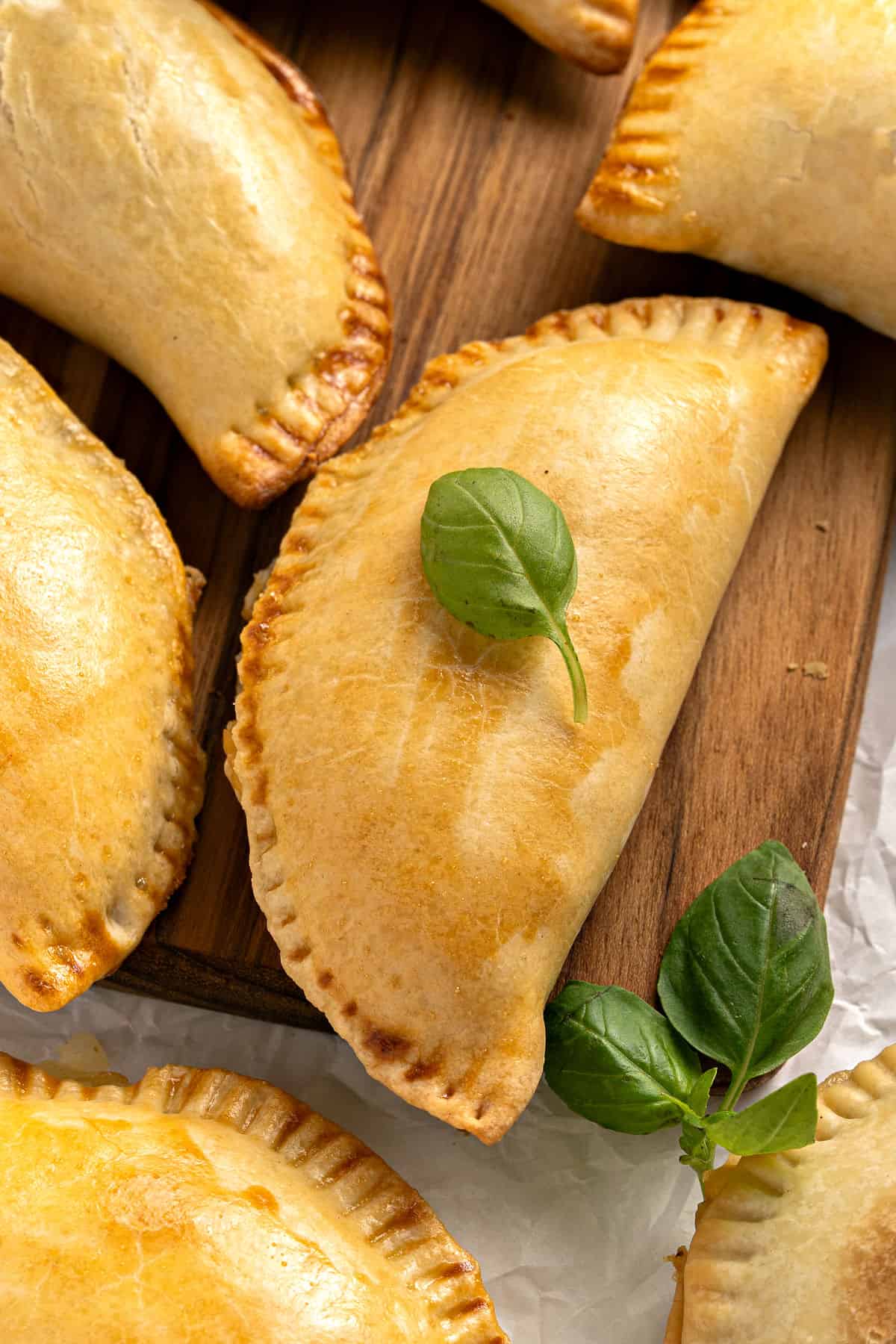 Close up corn empanadas with basil leaves on a wooden board.
