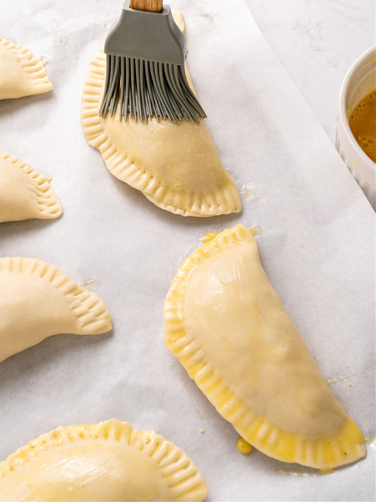 Brushing empanadas on parchment paper with egg wash.