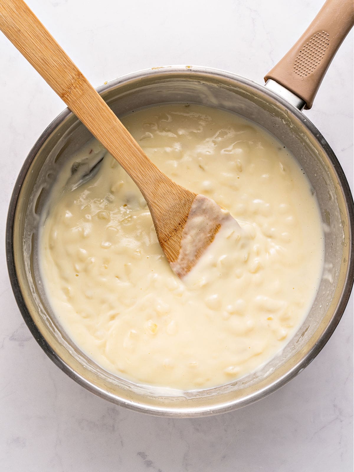 White sauce with onion in a metal saucepan. White background.