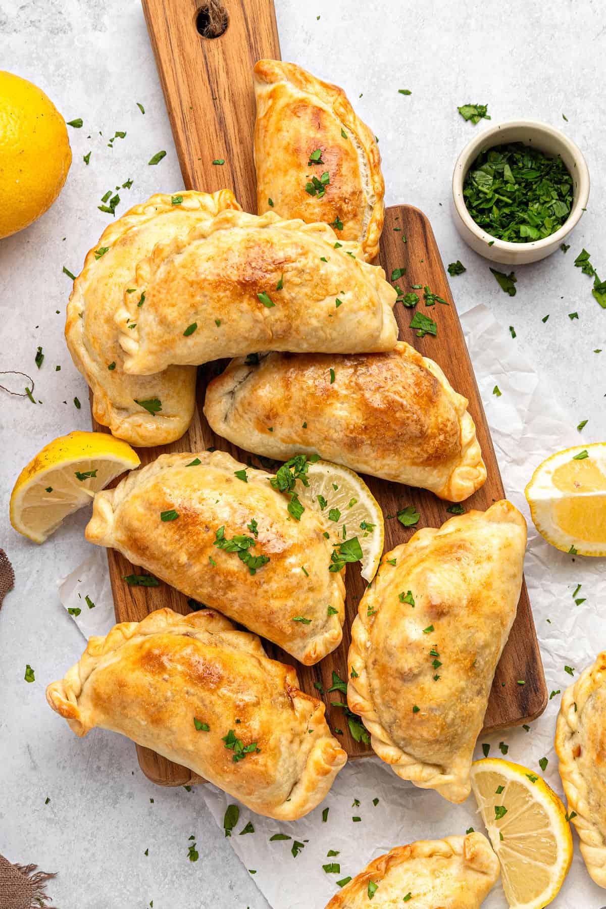 Corn Basil Handpies Top view of empanadas on a wooden board. Light gray background, chopped parsley.