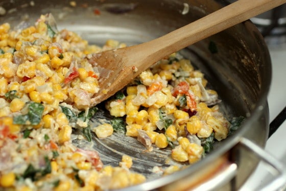 Corn empanada filling being cooked in a skillet with a wooden spoon. 