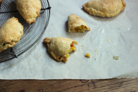 Whole and halved corn empanadas on parchment paper and on a wire rack. View from above.