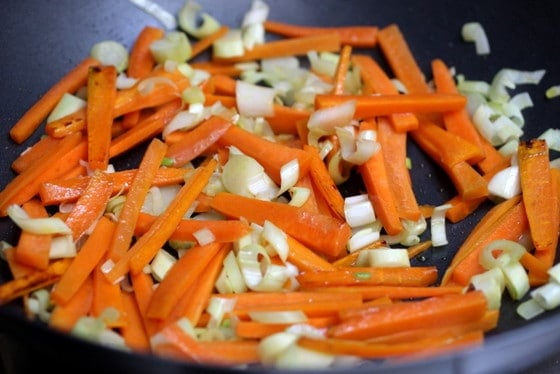 Lightly sauteeing onions and carrots in a wok.