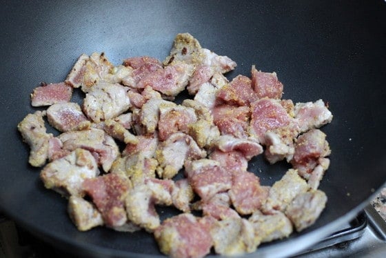 Cooking pork bits in a dark metal wok.