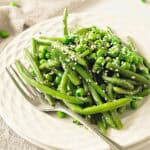 White plate with sesame green beans and peas. Silver fork. Close up view.