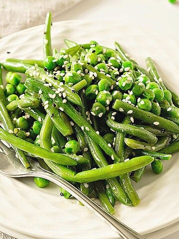 White plate with sesame green beans and peas. Silver fork. Close up view.