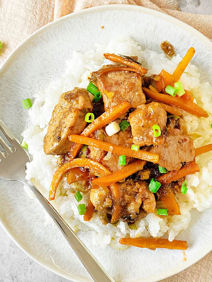 Close up of grayish plate with rice and pork carrot stir fry. Silver fork.