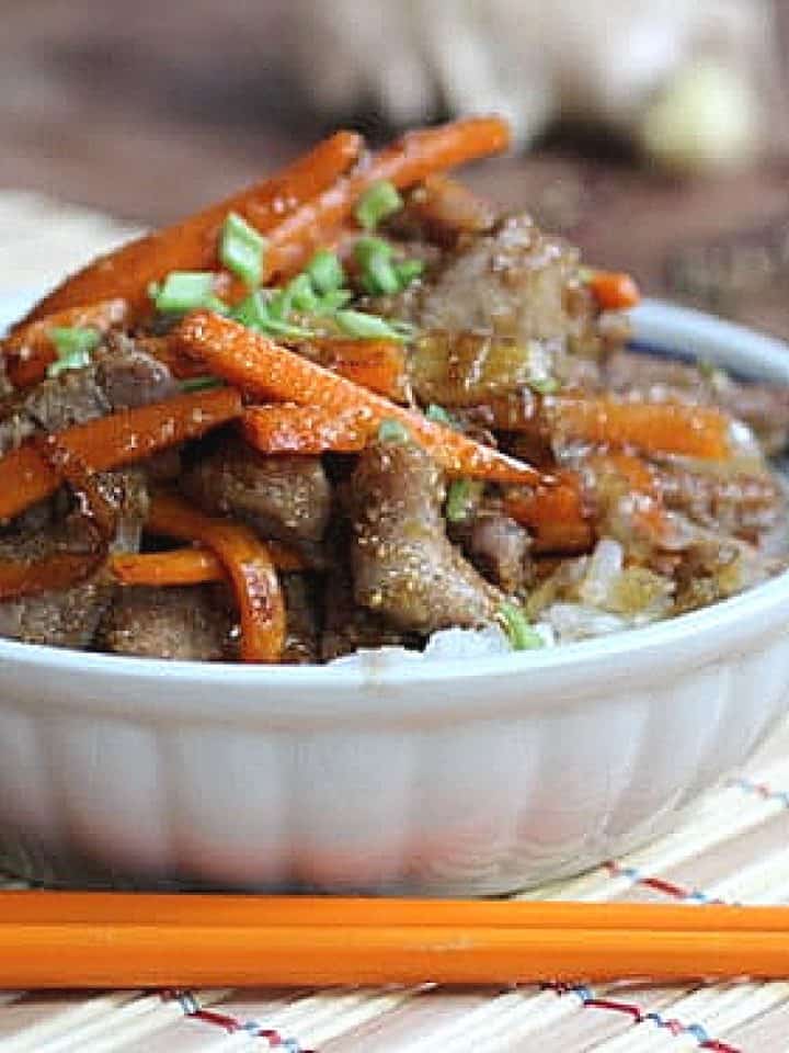 Close up of white bowl with pork and carrot stir fry on bamboo place mat.