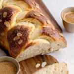 Braided bread with sliced almonds on a wooden board, white background. Coffee cups.