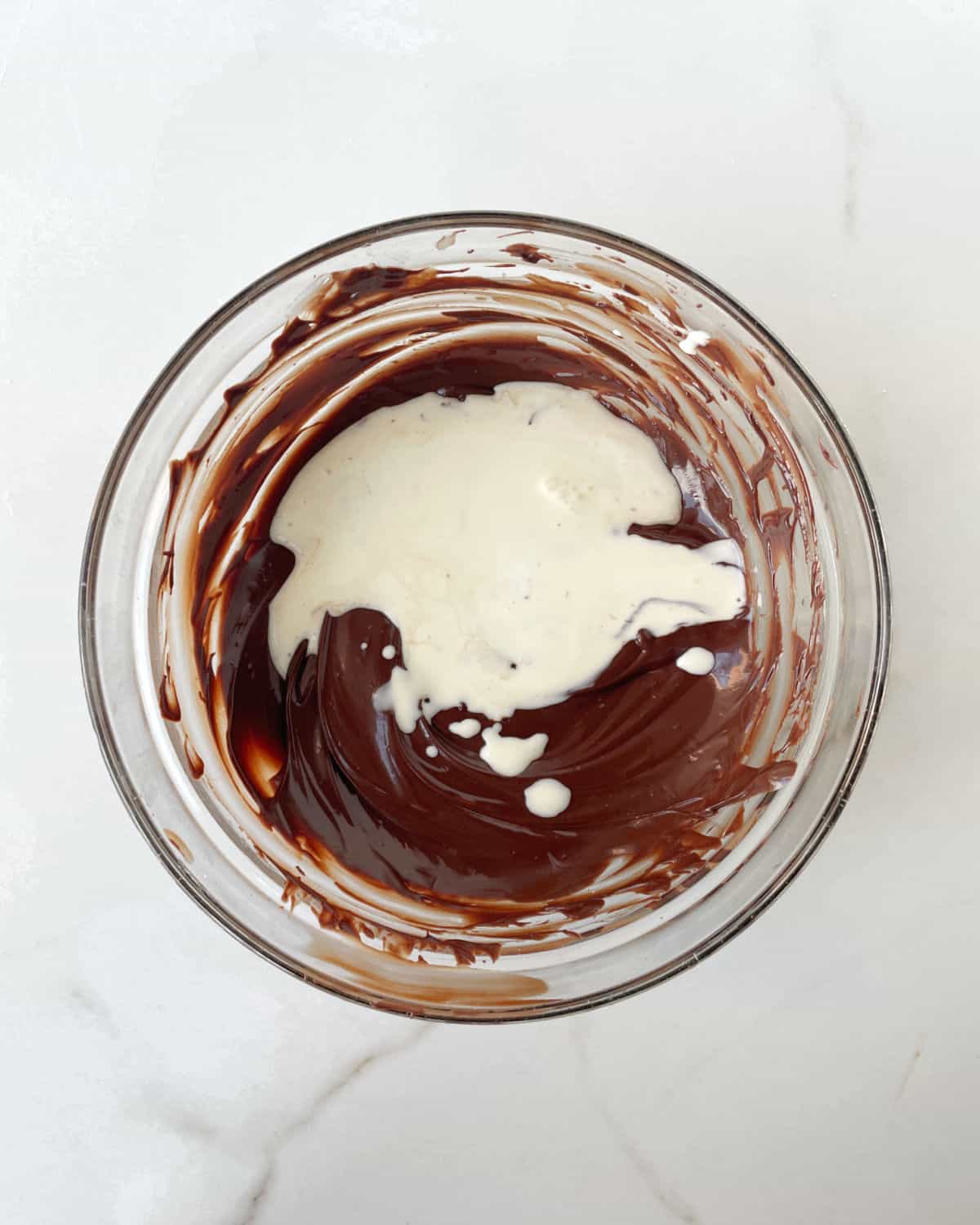 Glass bowl with melted chocolate and splash of cream on a white surface.