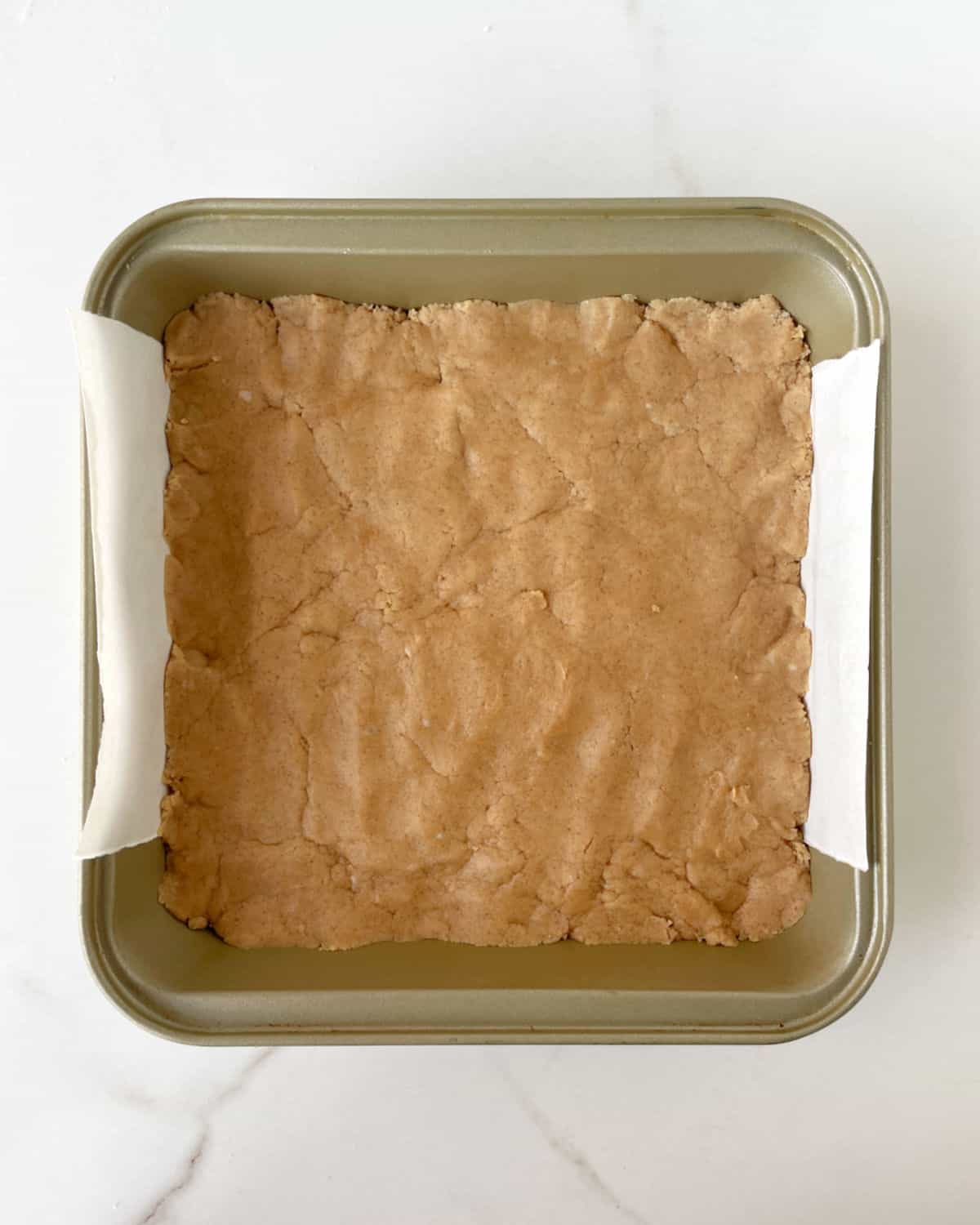 Peanut butter fudge layer on a gold colored square pan on a white marble surface.