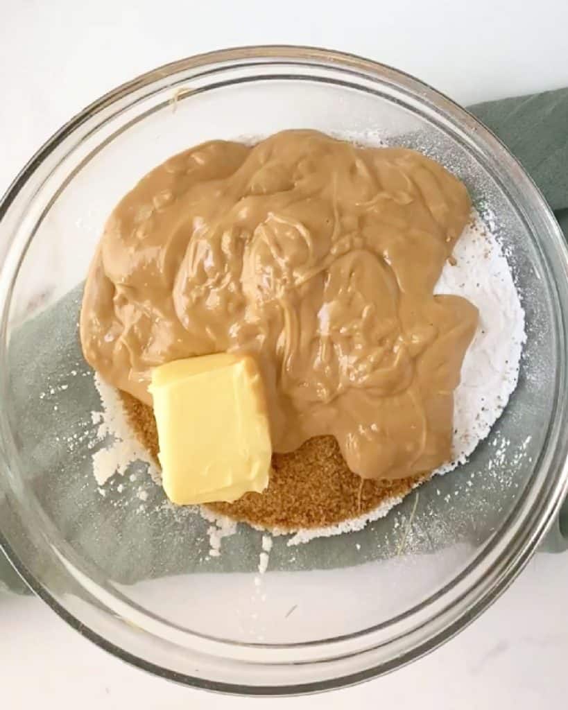 Peanut butter, butter, and powdered sugar in a glass bowl on a green cloth and white surface.