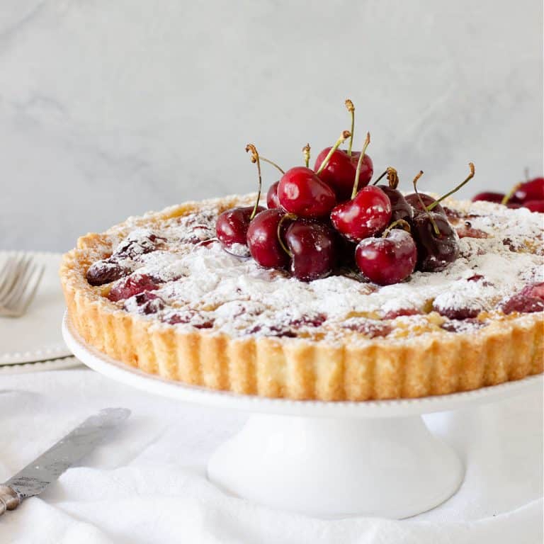 Front view of cherry tart on white cake stand, grey background