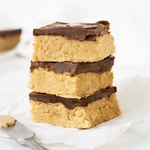 Three squares of peanut butter chocolate fudge on a white paper and white surface.