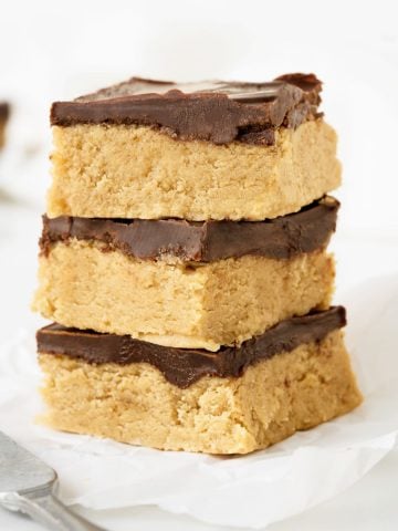 Three squares of peanut butter chocolate fudge on a white paper and white surface.