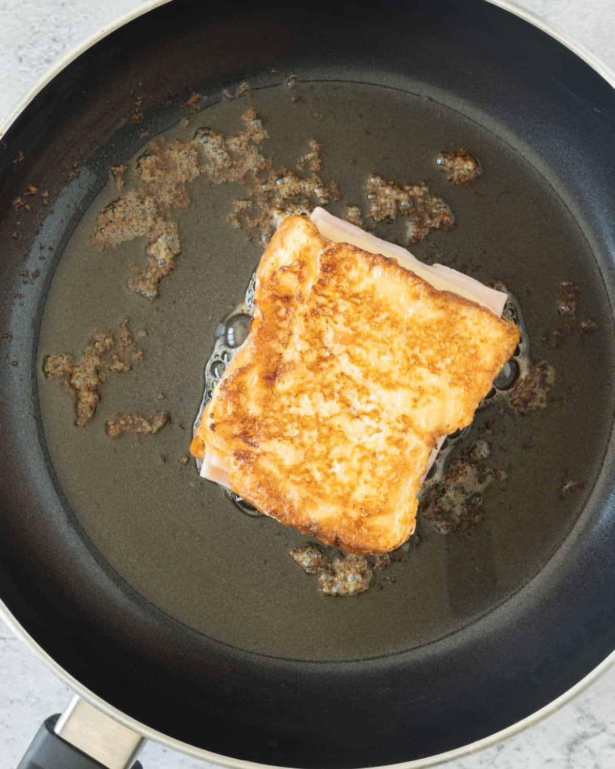Cooking a ham and cheese French toast sandwich on a black skillet.