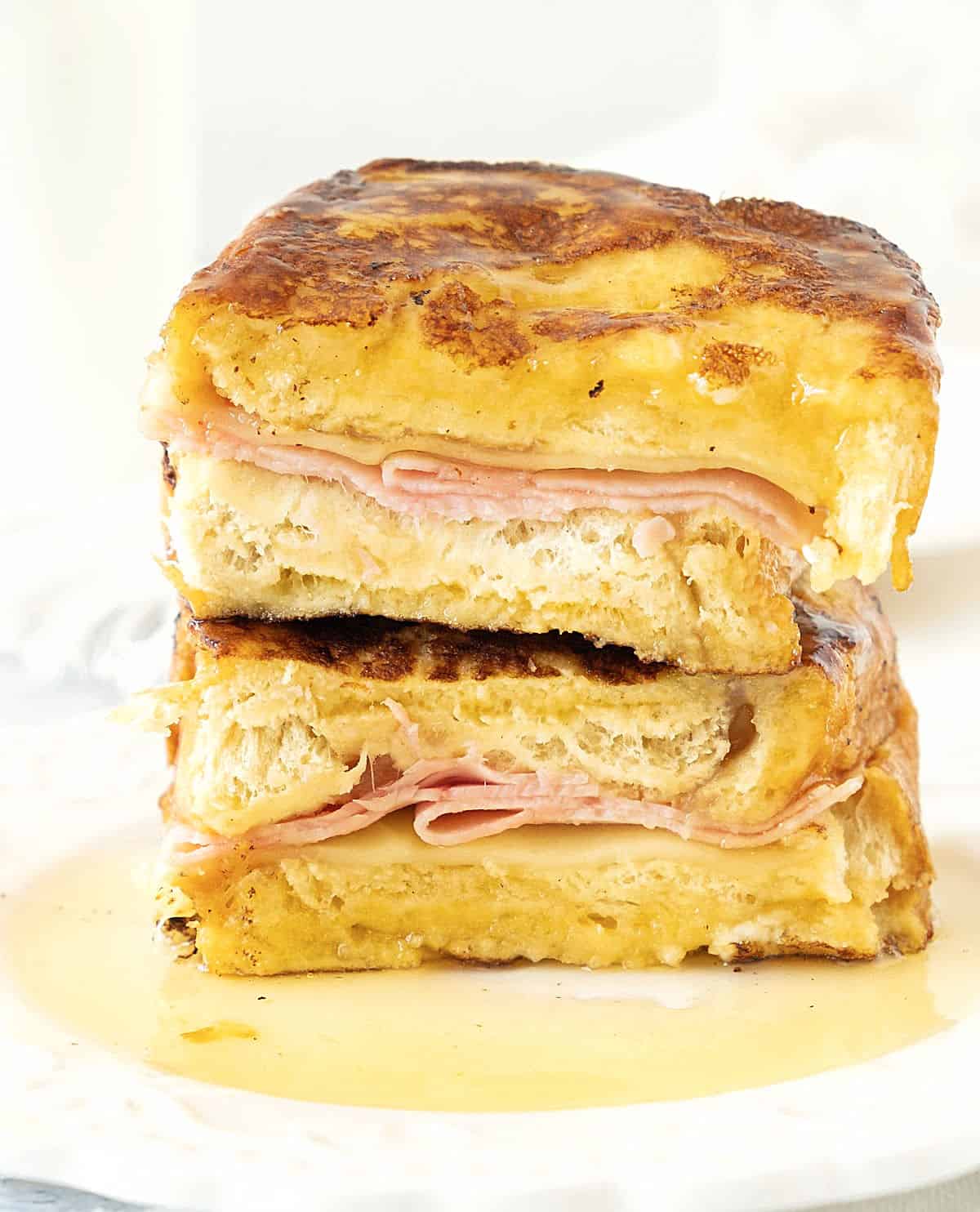 Halved ham and cheese French toast on a white plate with maple syrup. White background.