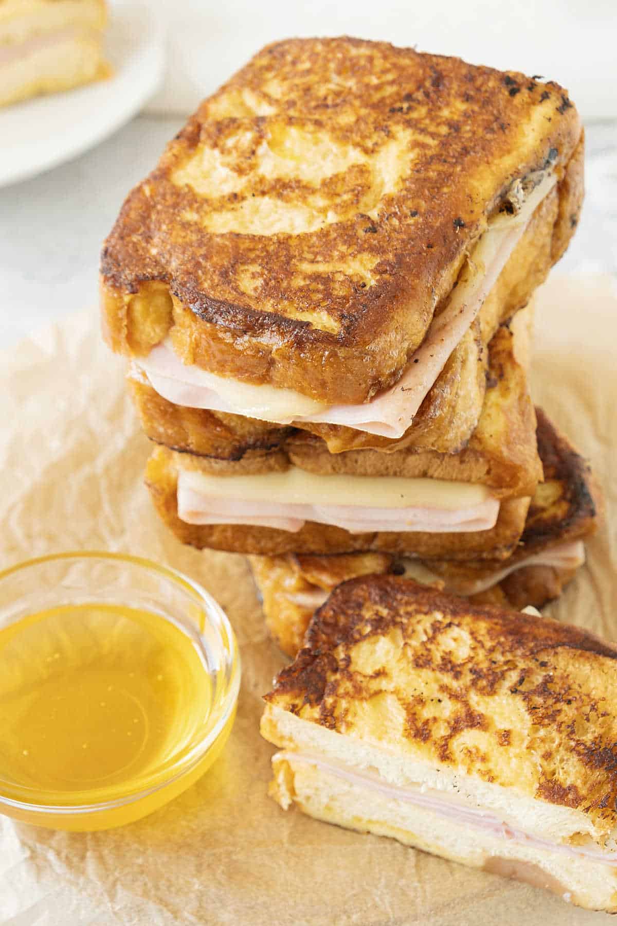 Stack of three Monte Cristo sandwiches and one half on beige parchment paper. A bowl with syrup. 