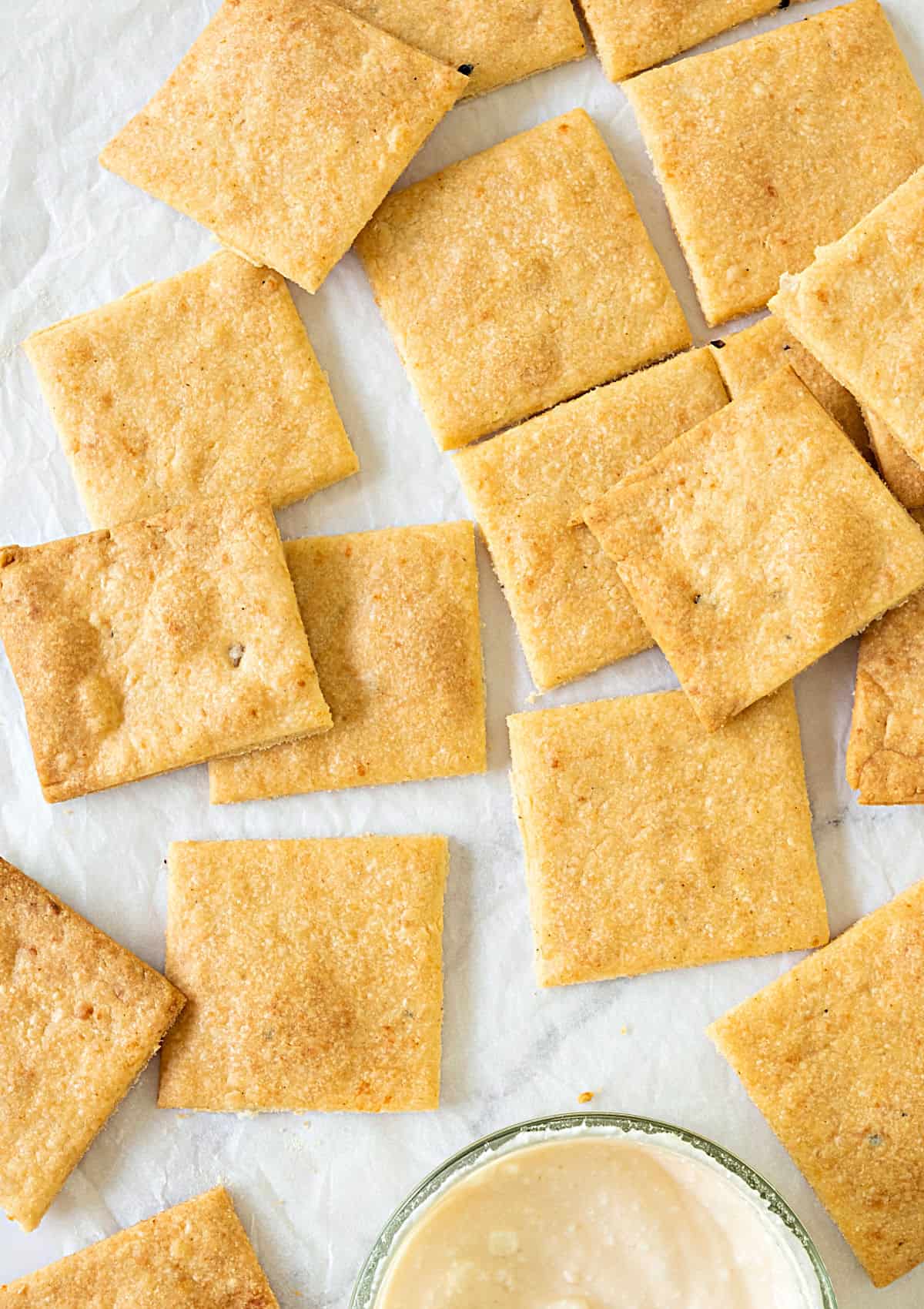 Several cheese crackers on a white surface. Bowl with white dip. Top view.