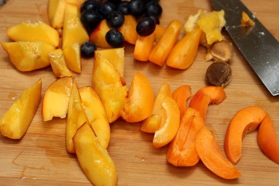 Light wooden board with knife and apricot and peach wedges, and blueberries.