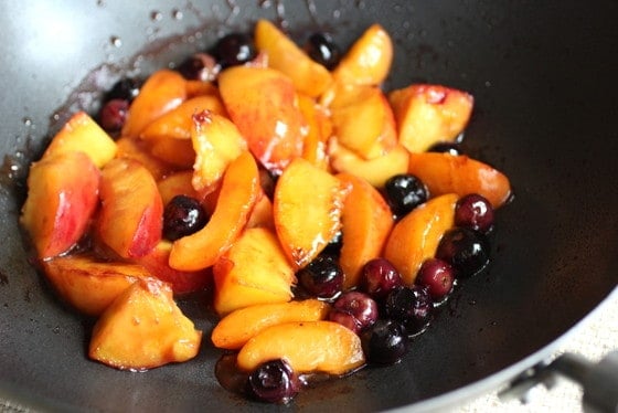 Caramelized summer fruit on a dark metal wok.