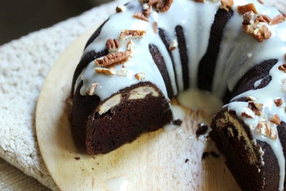 On a wooden plate a Chocolate Bundt Cake with several missing slices.