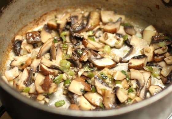 Metal skillet with cooked sliced mushrooms and green onion.
