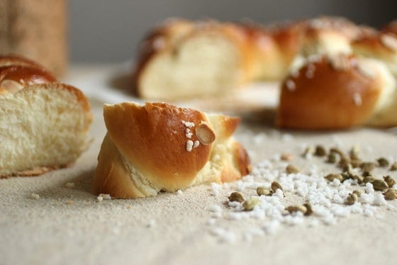 Cut piece of pulla bread, with whole bread in background; cardamom pods