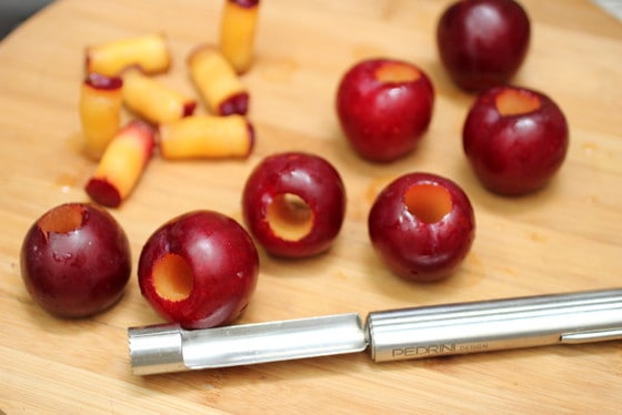 Plums, whole and cored on a wooden board with an apple corer.