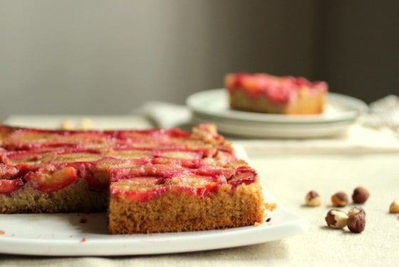 Partial view of plum cake on white platter with more plates and cake in background.