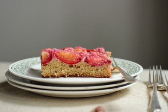 Square of plum cake on stack of white and green plates with silver forks. 