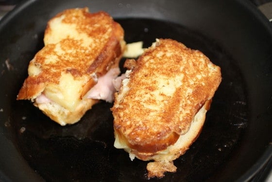 Cheese and ham stuffed french toast being cooked on a dark skillet. 