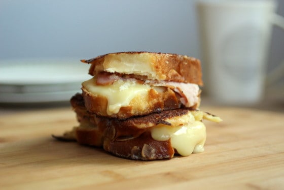 Two cheese stuffed french toast sandwiches stacked on a wooden board. 