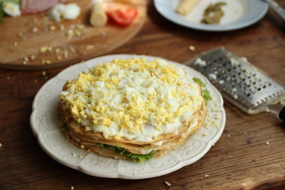 Grating hard boiled eggs to crepe cake, white plate, grater, wooden table.