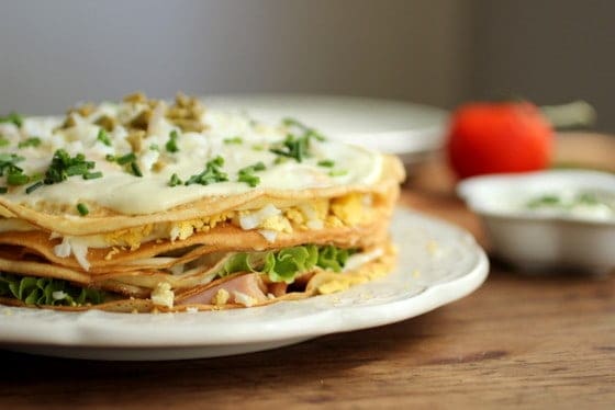A savory Crêpe Cake with mayonnaise and egg on a white plate, wooden table.