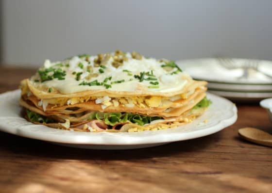 Front view of finished Savory Crêpe Cake on a white plate, wooden table.