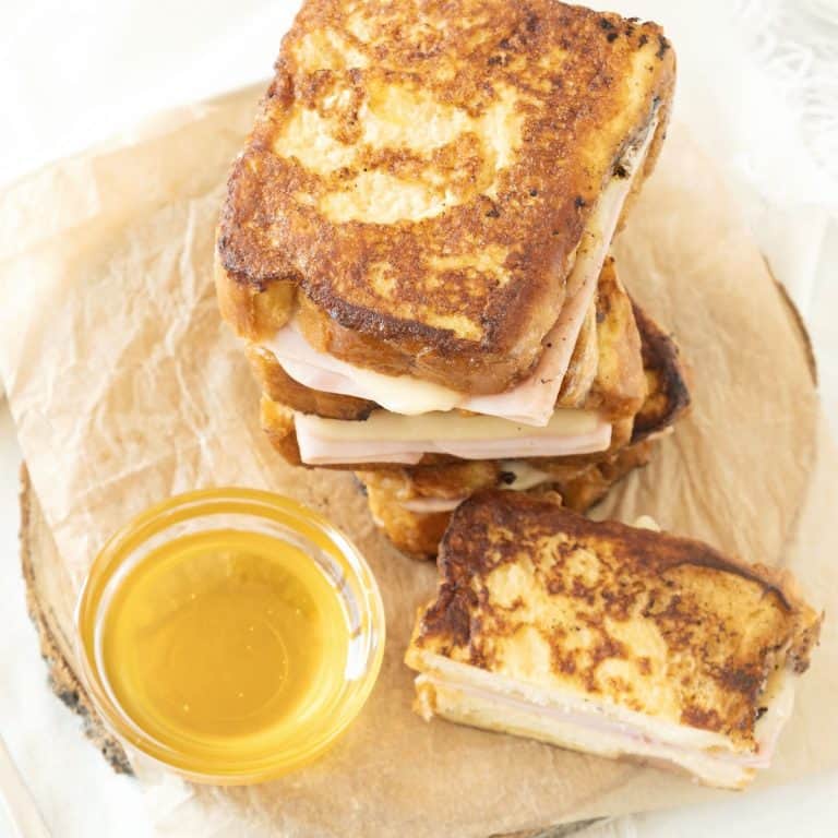 Top view of stack of ham and cheese French toast on beige parchment paper. A bowl with syrup.