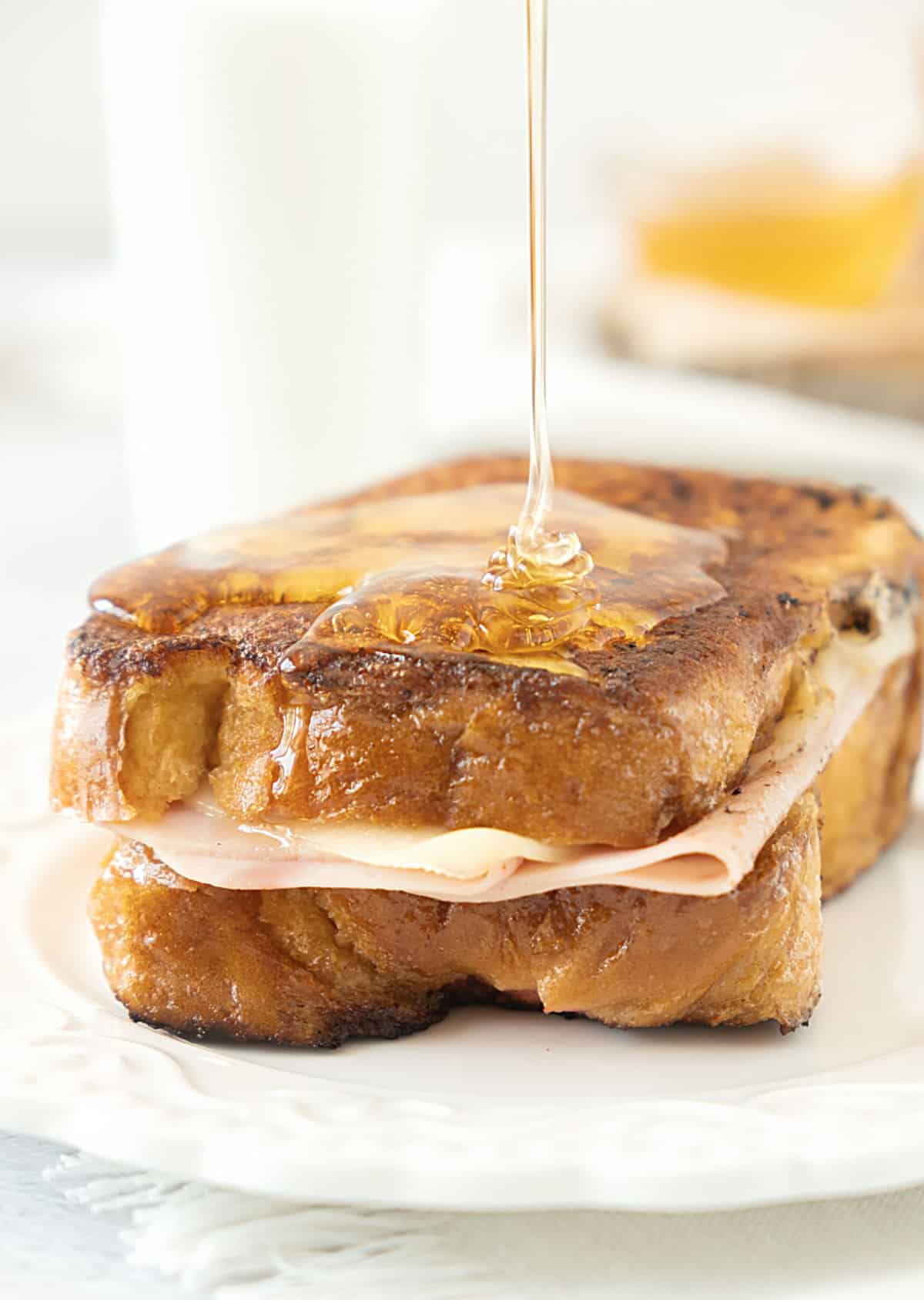 Drizzling maple syrup on a Monte Cristo sandwich on a white plate. White background. 