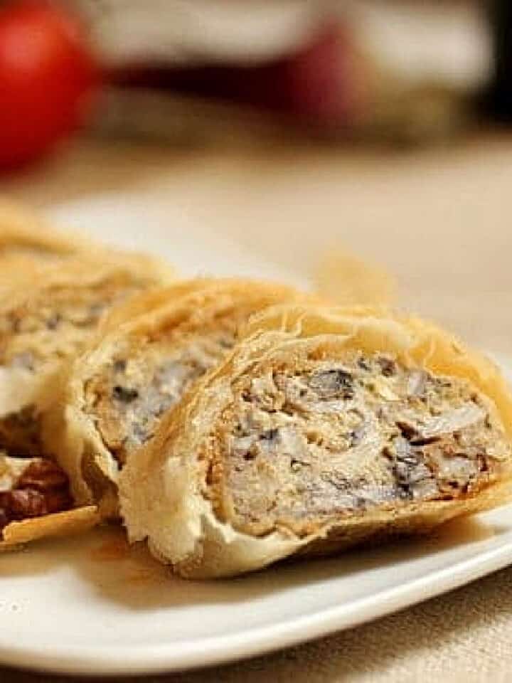 Slices of mushroom strudel on a white plate with beige surface.